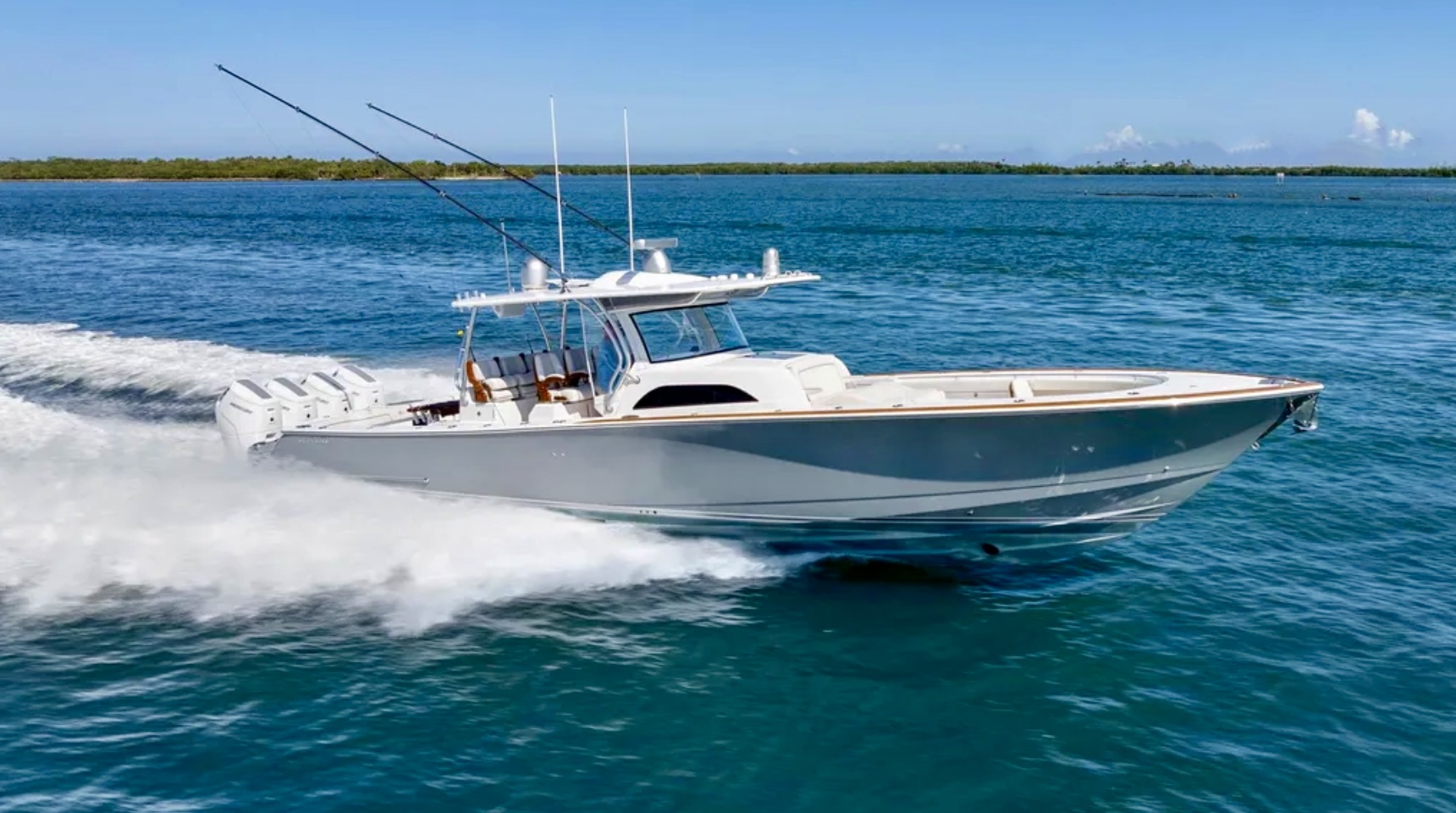 A sleek motorboat with four engines is speeding across clear blue water under a clear sky.