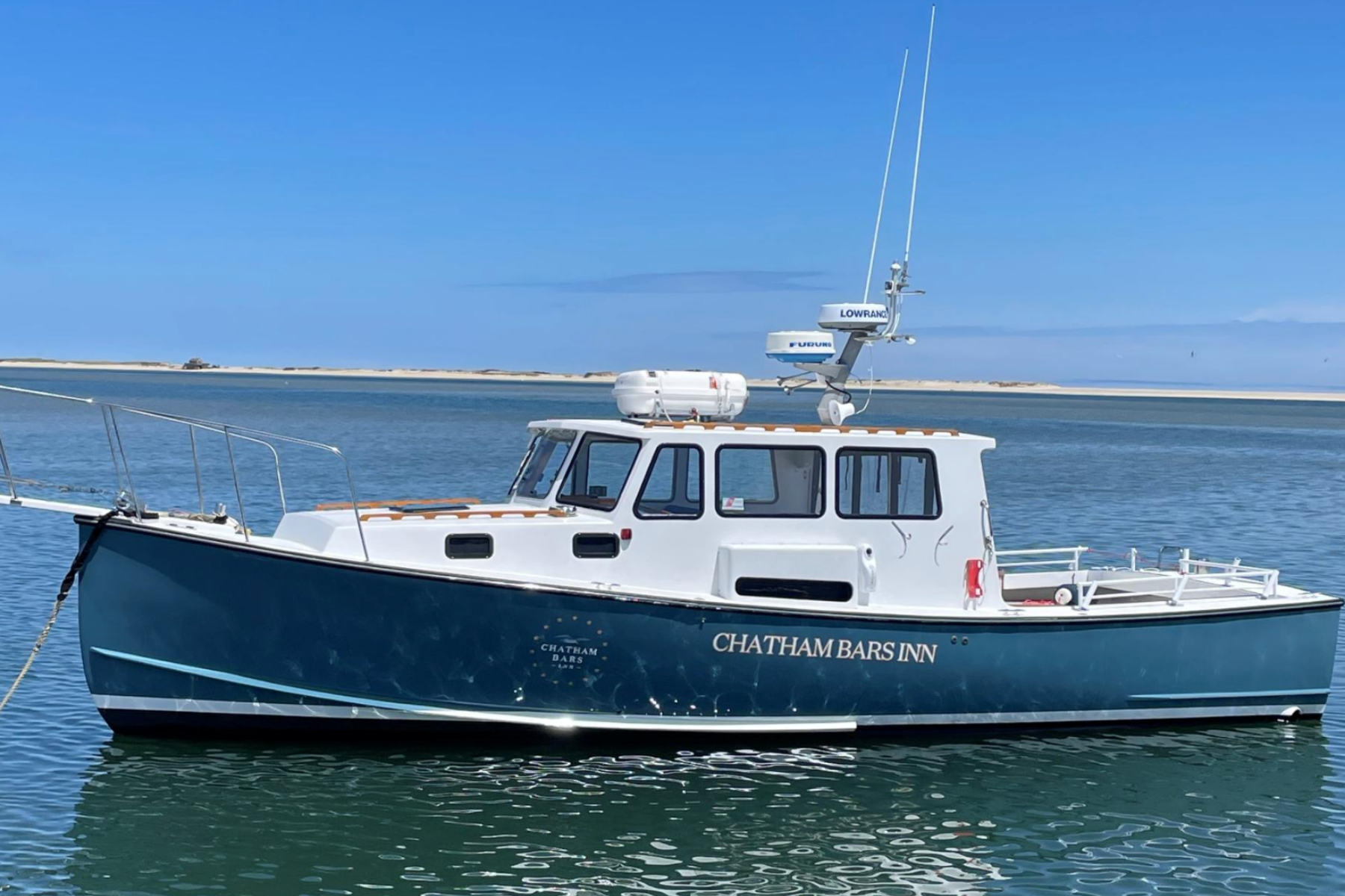 The image shows a boat named "Chatham Bars Inn" on calm water with a sandy shoreline and a blue sky in the background.