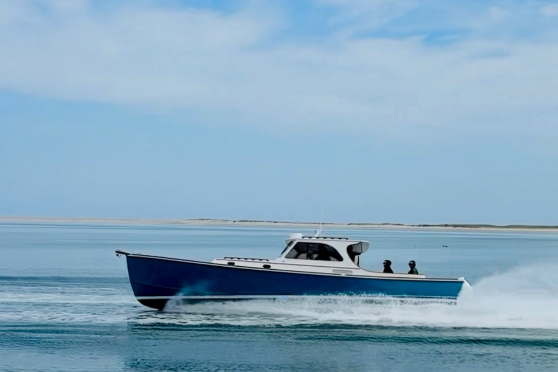 A motorboat is speeding across a calm blue sea under a partly cloudy sky in this image.