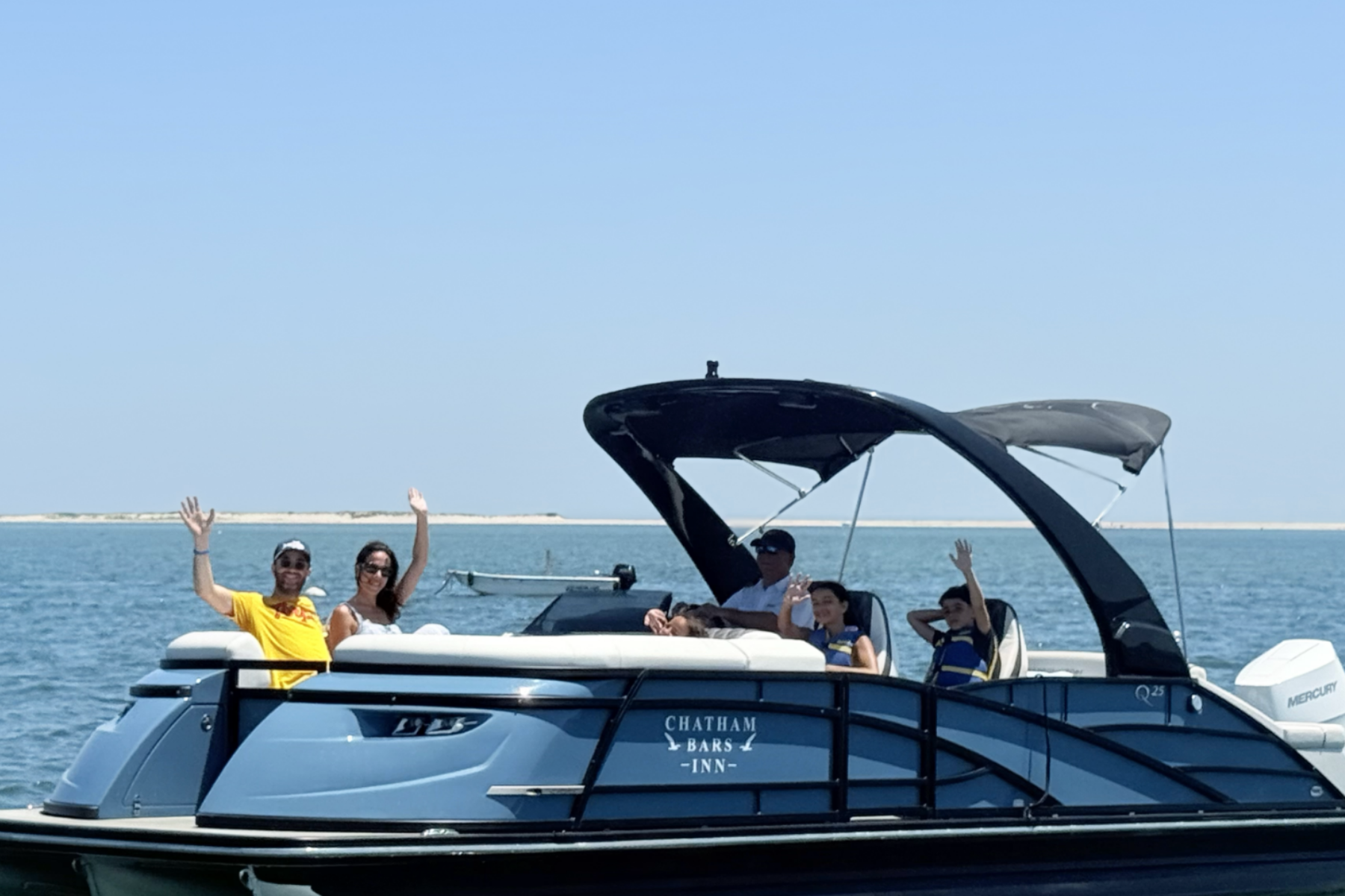 A group of people waving from a boat labeled "Chatham Bars Inn" on a sunny day, with the ocean and a distant shoreline in the background.