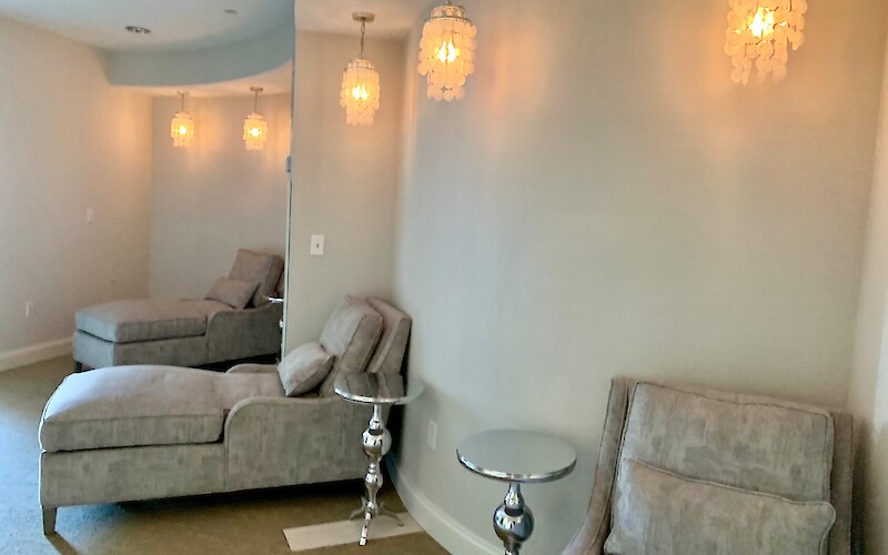 The image shows a cozy lounge area with gray chaise lounges, side tables, and hanging pendant lights on the wall.