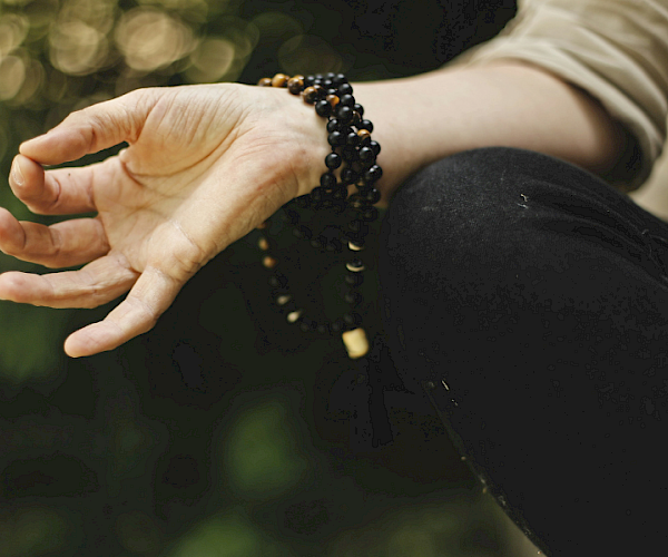 A hand holding a string of black and brown beads, possibly in a meditative or peaceful outdoor setting.