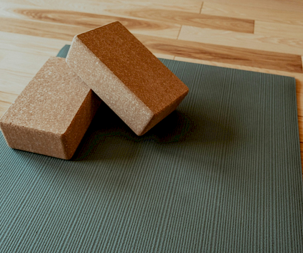Two cork yoga blocks on a green yoga mat, placed on a wooden floor, ready for a calm and focused practice.