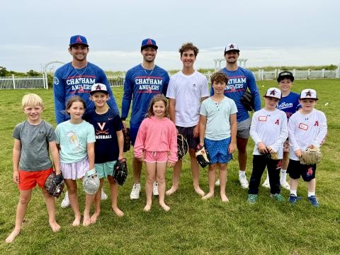 A group of kids with baseball gloves and balls pose with adults in matching "Chatham Anglers" shirts and hats on a grassy field.