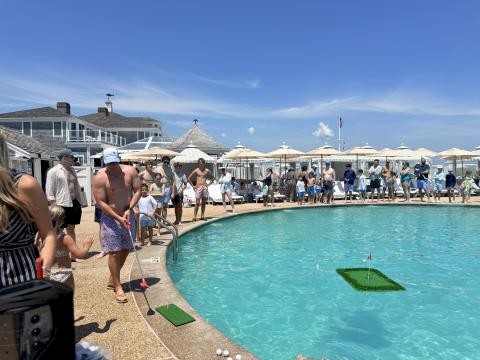 People are gathered around a pool, watching a person play golf, aiming at a floating target.