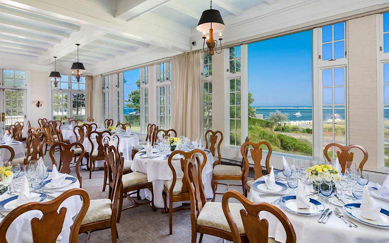 A beautifully set dining room with elegant tables and chairs overlooking a scenic ocean view through large windows.