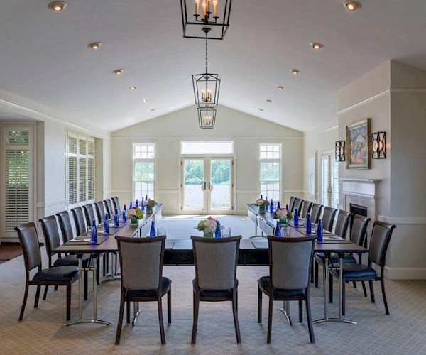 A conference room with a U-shaped table, chairs, blue water bottles, and floral centerpieces, with large windows and modern lighting.