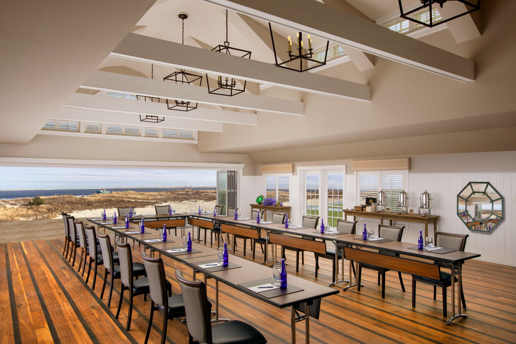 A spacious conference room with rows of tables and chairs, water bottles placed on each table, overlooking an open scenic view.