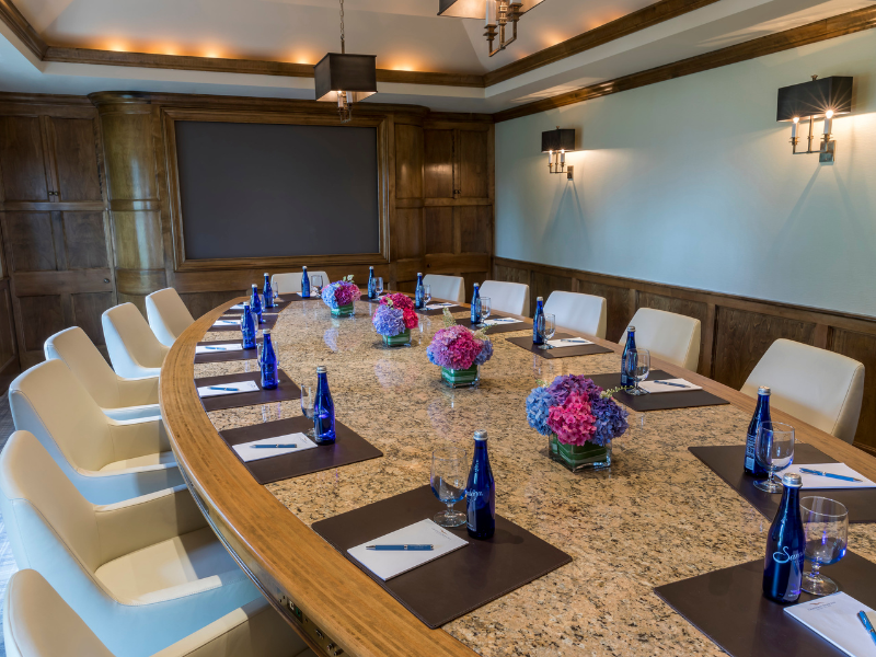 A conference room with a large oval table, set with notepads, pens, water bottles, and flower arrangements.