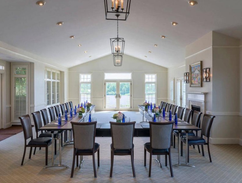 A U-shaped conference room setup with chairs, tables, blue water bottles, and decorative elements including wall art and lighting fixtures.