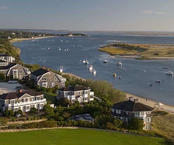 Coastal view with waterfront houses, a calm bay, several small boats, and an island in the background.