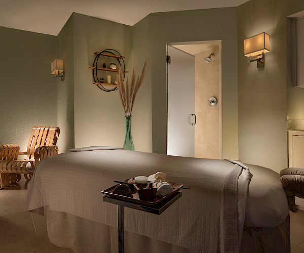 A spa room with a massage table, soft lighting, chair, and decorative items, creating a relaxing atmosphere.