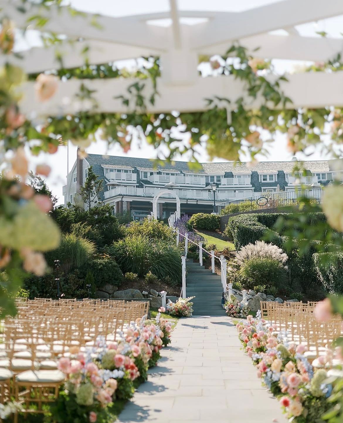 An outdoor wedding setup with chairs and floral arrangements along a walkway, leading to a building in the background.