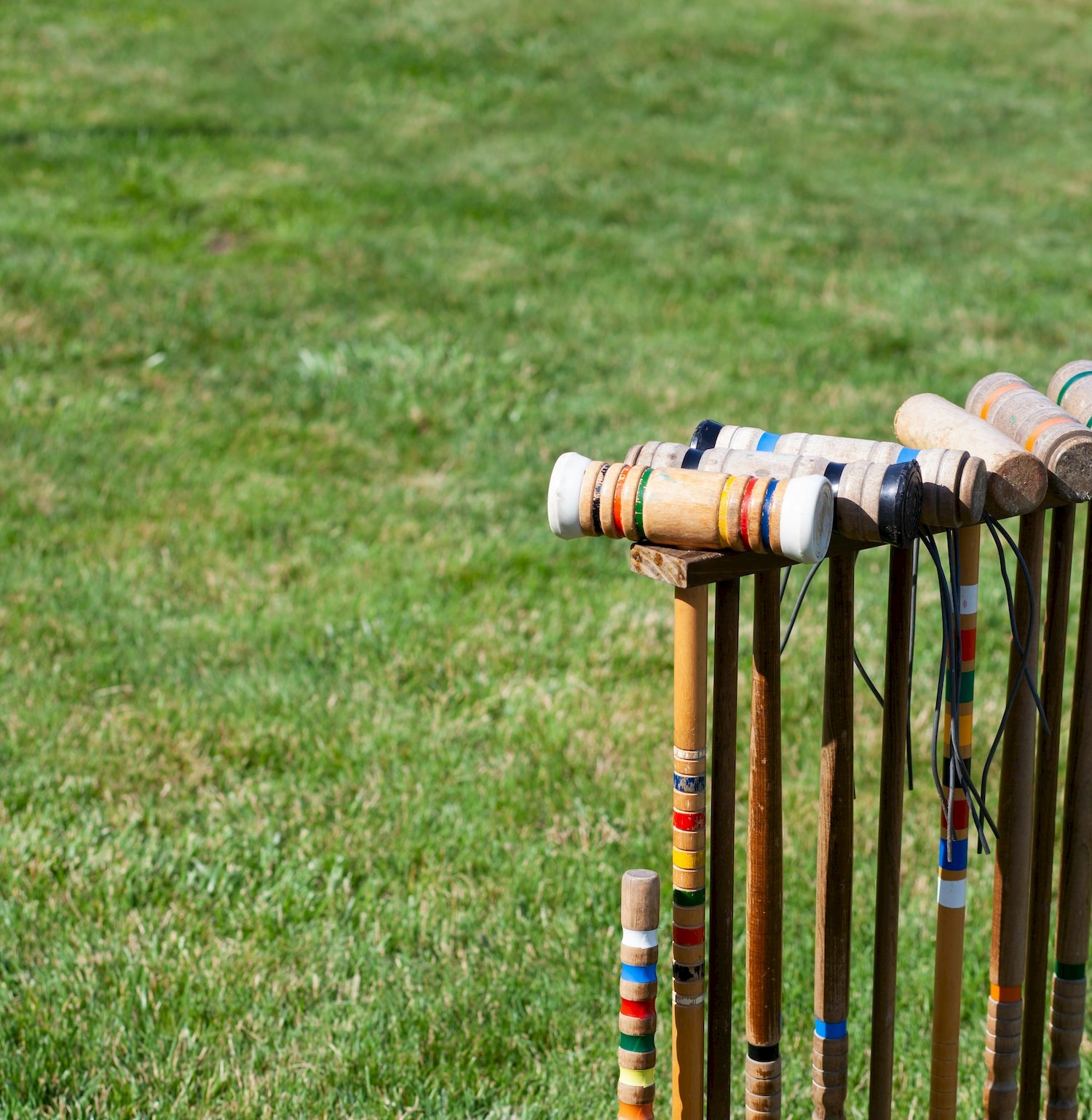 A set of colorful croquet mallets and stakes is positioned on a grassy field.