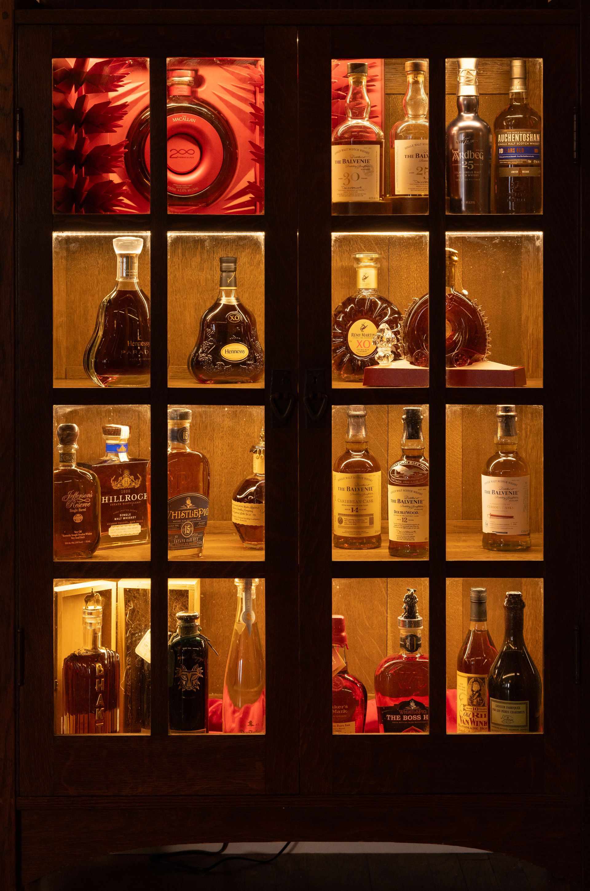 A wooden cabinet with glass doors displaying a variety of liquor bottles, including whiskey and cognac.
