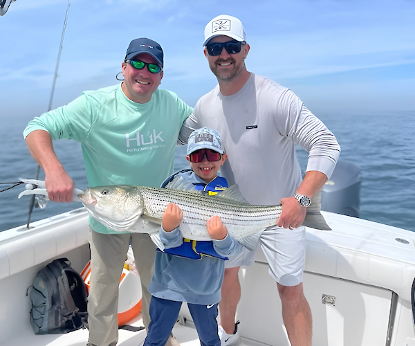 Two adults and a child on a boat holding a large fish, smiling at the camera.
