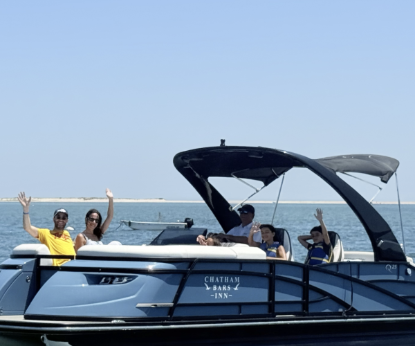 A group of people on a boat in the ocean, waving and smiling under a clear blue sky.