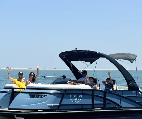 A group of people on a boat in the ocean, waving and smiling under a clear blue sky.