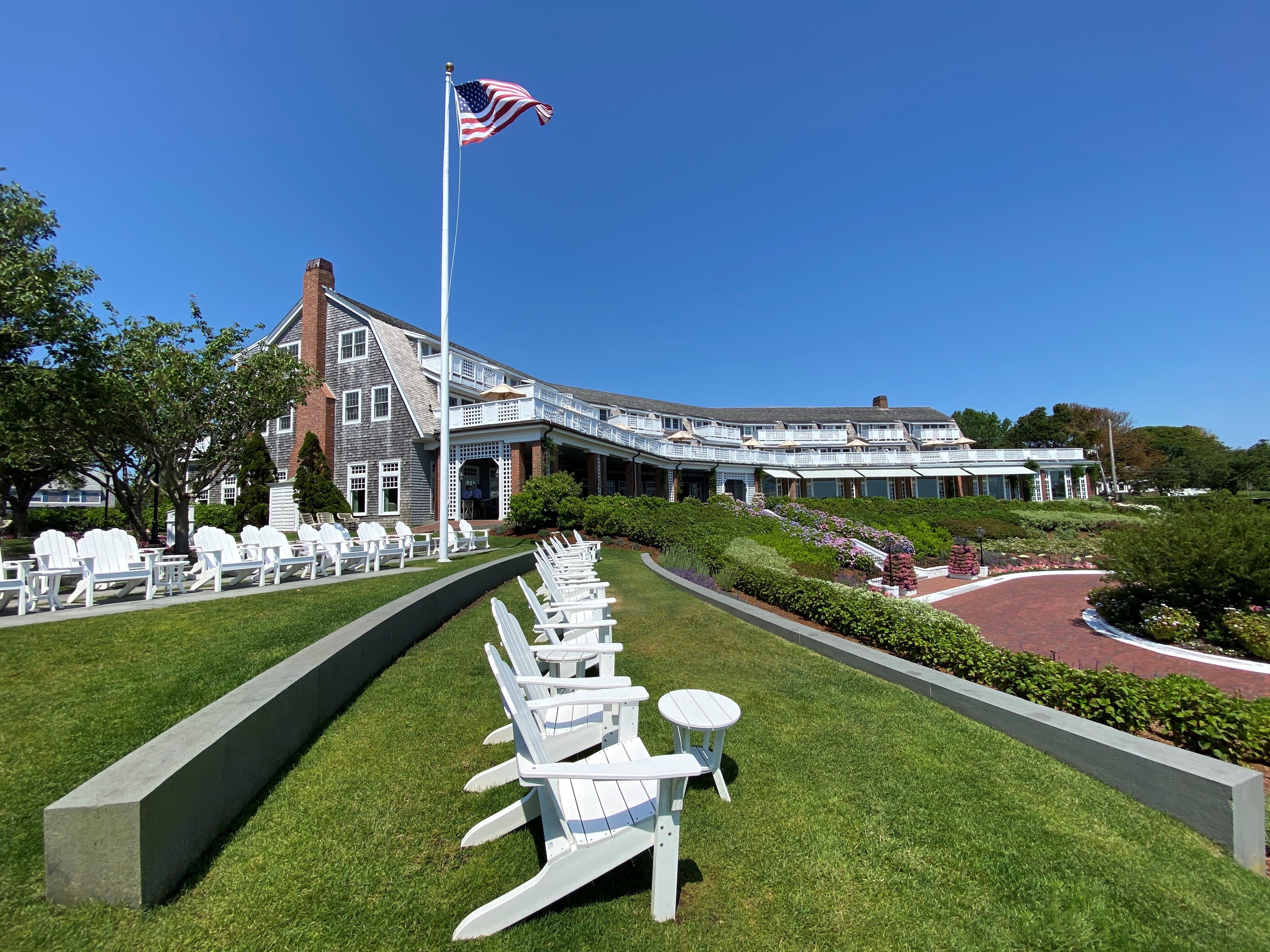 A large building with a U.S. flag, manicured lawn, white chairs, and clear blue sky in a garden setting.