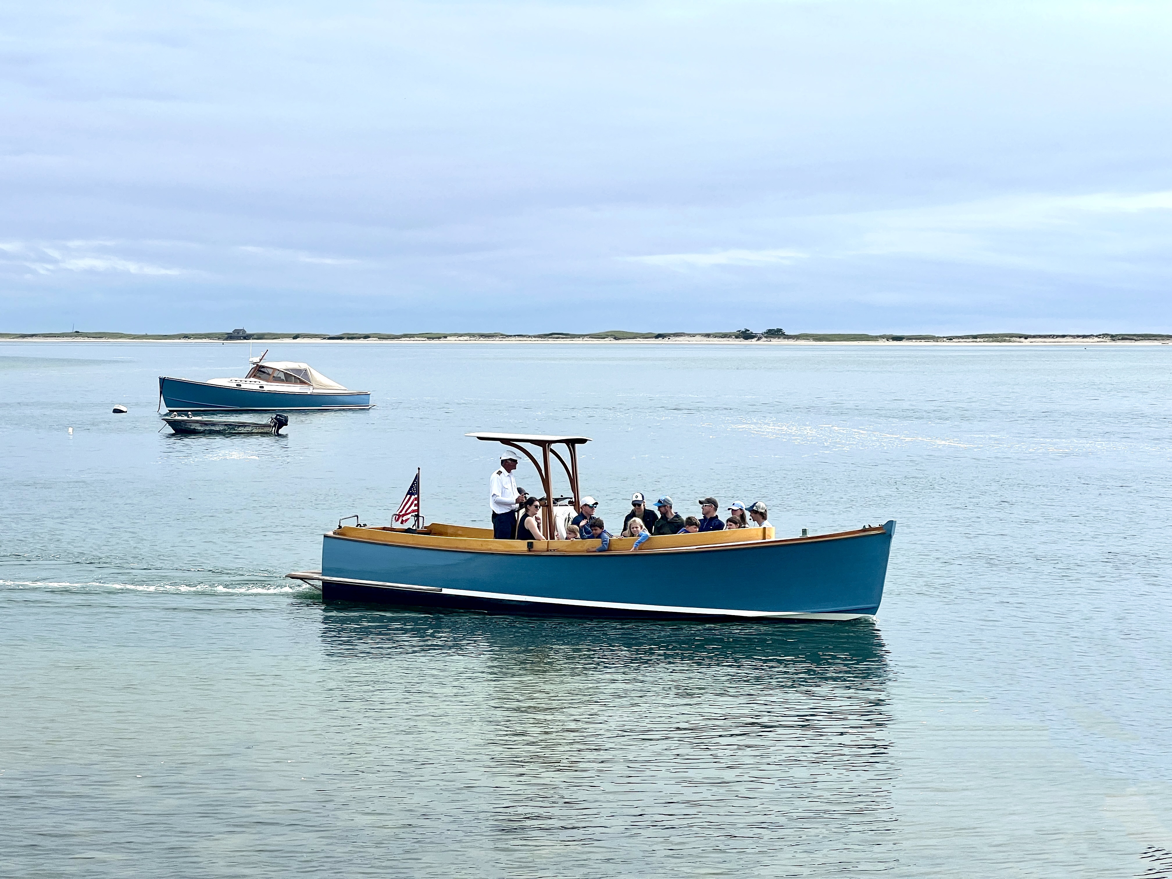 A boat with passengers is sailing on calm water, with another boat further away, under a cloudy sky.