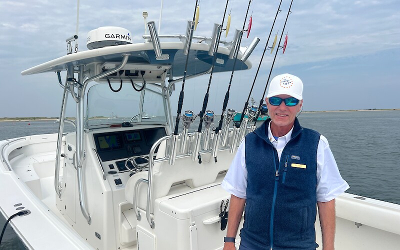 A person stands on a fishing boat with multiple rods, wearing sunglasses and a cap. The boat is equipped with navigation tech.