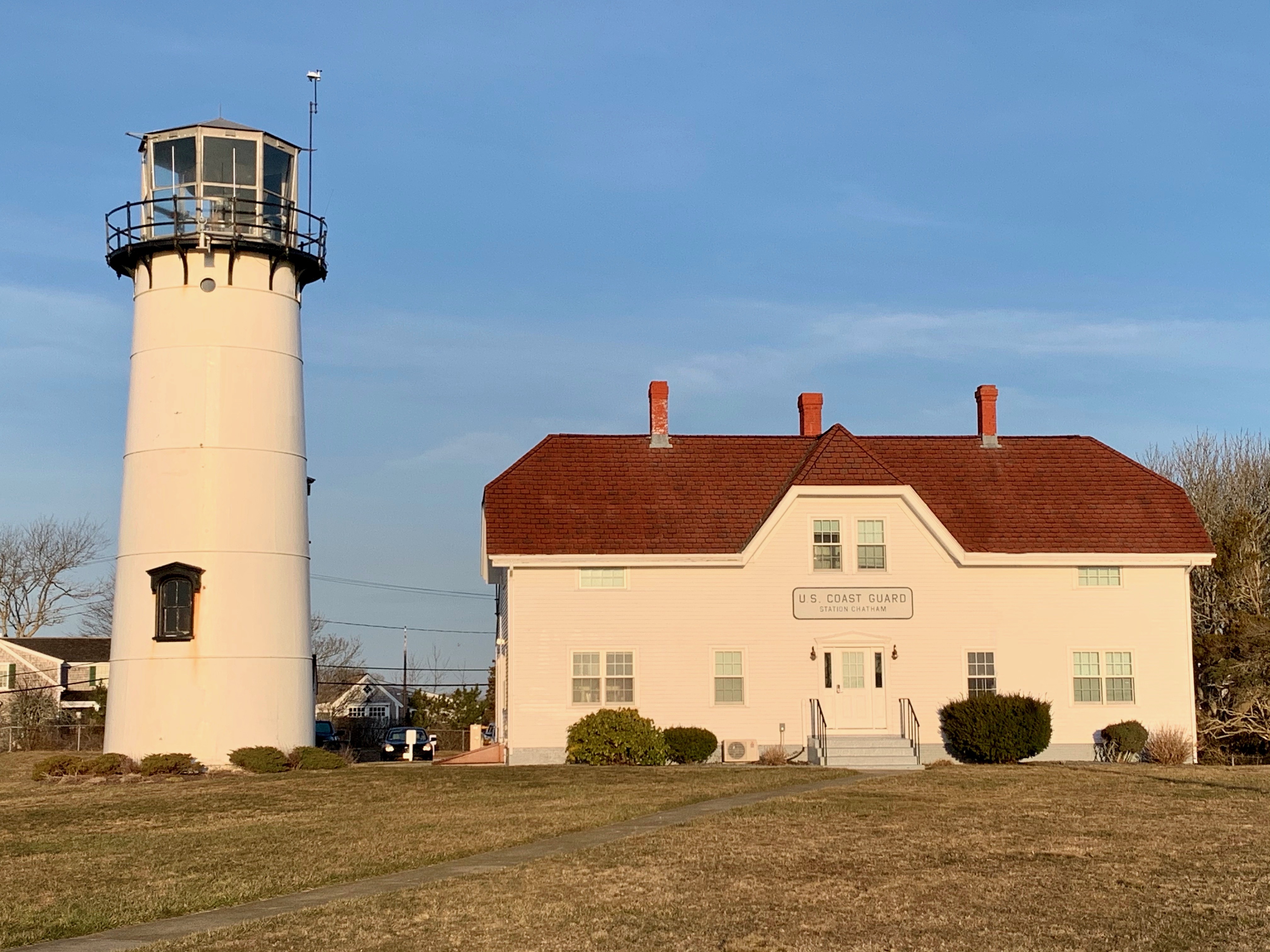 A lighthouse stands next to a building labeled "U.S. Coast Guard Station Chatham" under a clear blue sky.