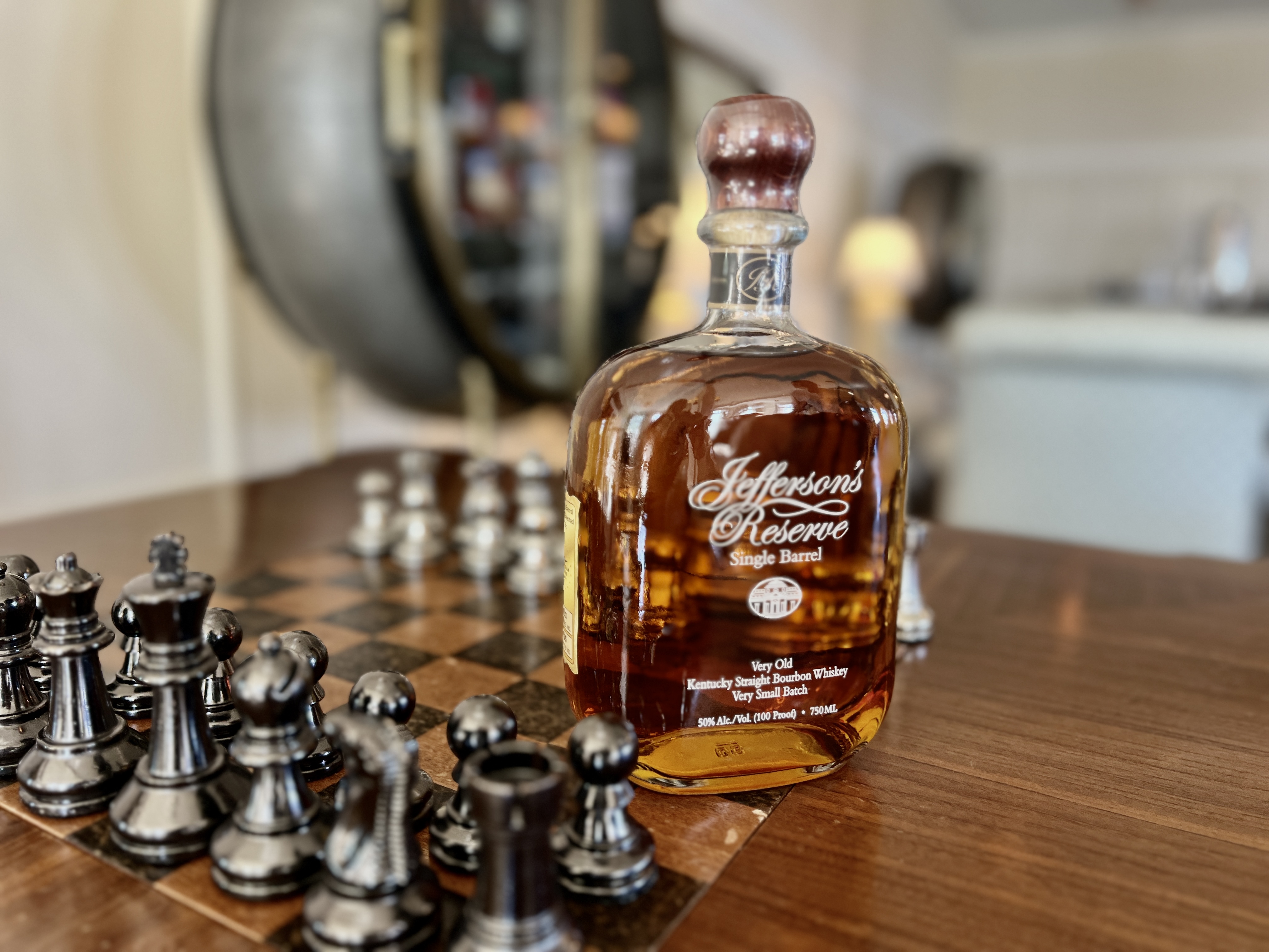 A bottle of Jefferson's Reserve Single Barrel bourbon sits on a wooden table next to a chessboard with silver chess pieces.