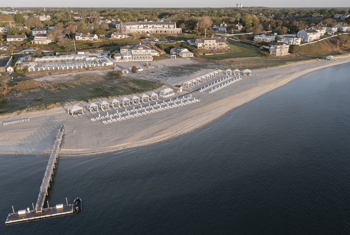 An aerial view of a beach resort with lined cabanas, umbrellas, and a dock extending into the ocean.