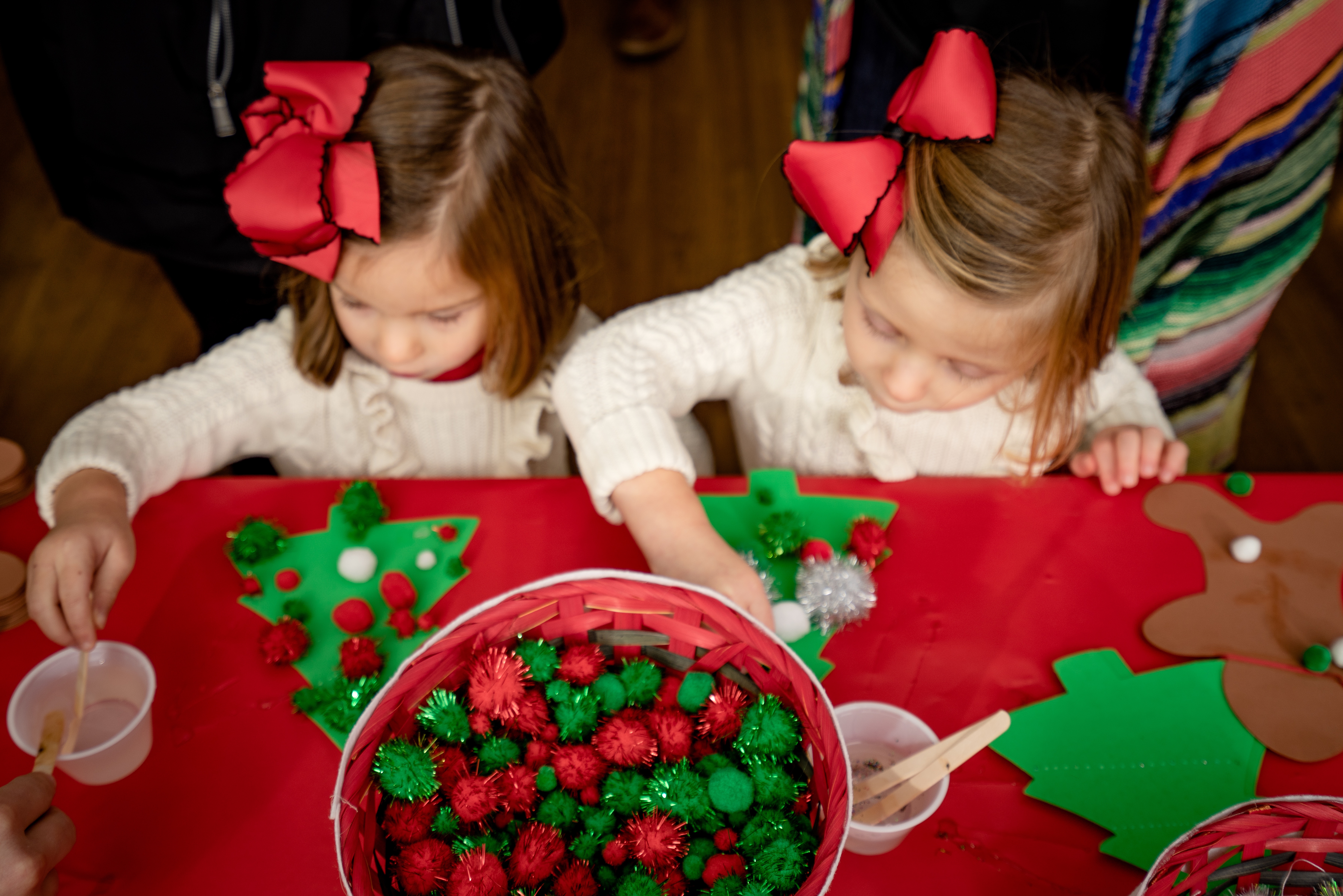 Two children are crafting with Christmas-themed materials on a red table.