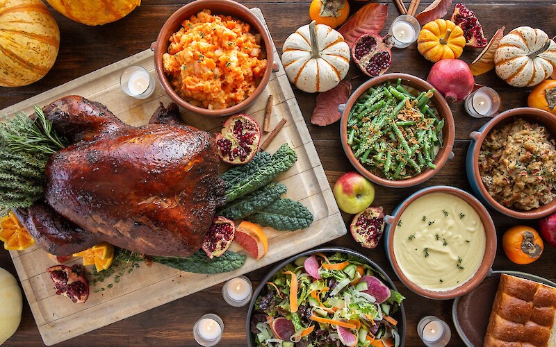 A Thanksgiving feast with roast turkey, mashed carrots, green beans, stuffing, salad, and seasonal decorations completes the table.