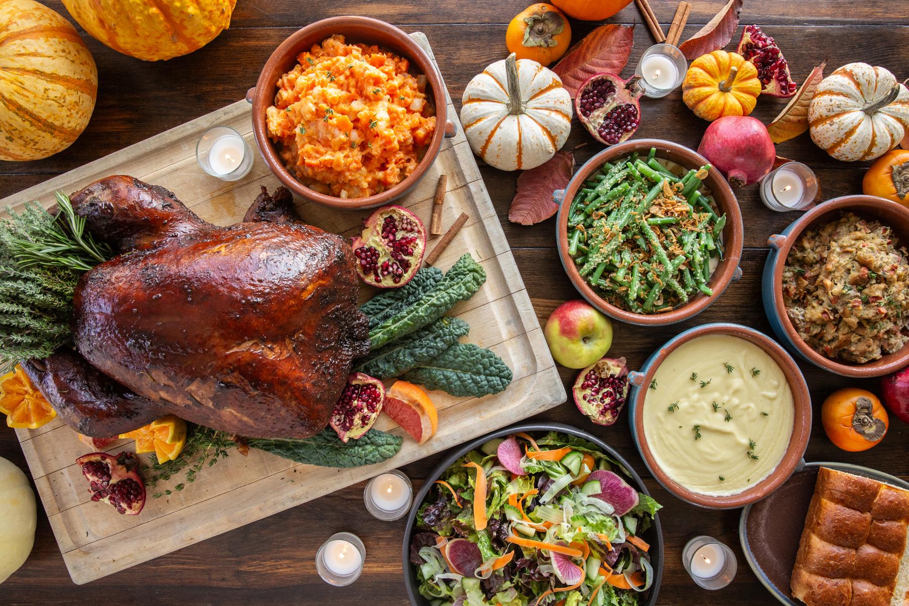 A Thanksgiving feast with turkey, mashed vegetables, green beans, salad, pomegranate, apples, pumpkins, squash, and candles.