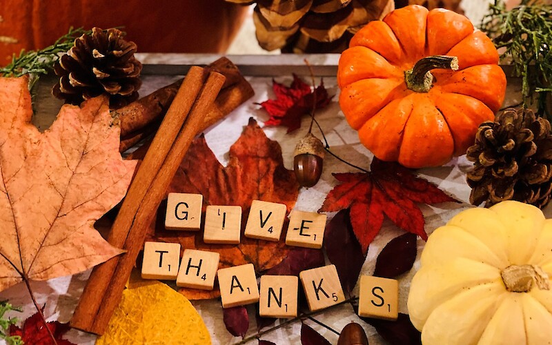 Autumn-themed setup with pumpkins, pine cones, cinnamon sticks, leaves, acorns, and scrabble tiles spelling "Give Thanks."