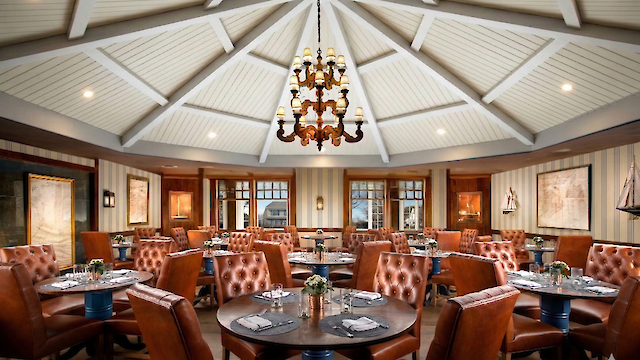 A restaurant dining area with round tables, brown leather chairs, a central chandelier, and decorative walls and ceiling.