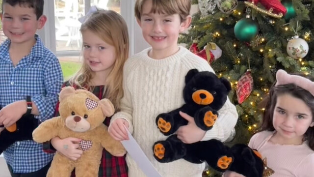 Children are standing in front of a Christmas tree holding stuffed animals, with festive decorations around.