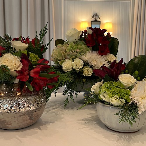 The image shows three floral arrangements featuring white roses, red lilies, green hydrangeas, and various greenery in decorative vases.