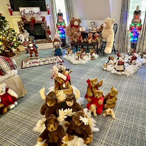 A festive room with Christmas decorations, teddy bears, nutcrackers, and a lit Christmas tree by a fireplace labeled "Merry Christmas."