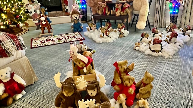 A festive room with Christmas decorations, teddy bears, nutcrackers, and a lit Christmas tree by a fireplace labeled "Merry Christmas."
