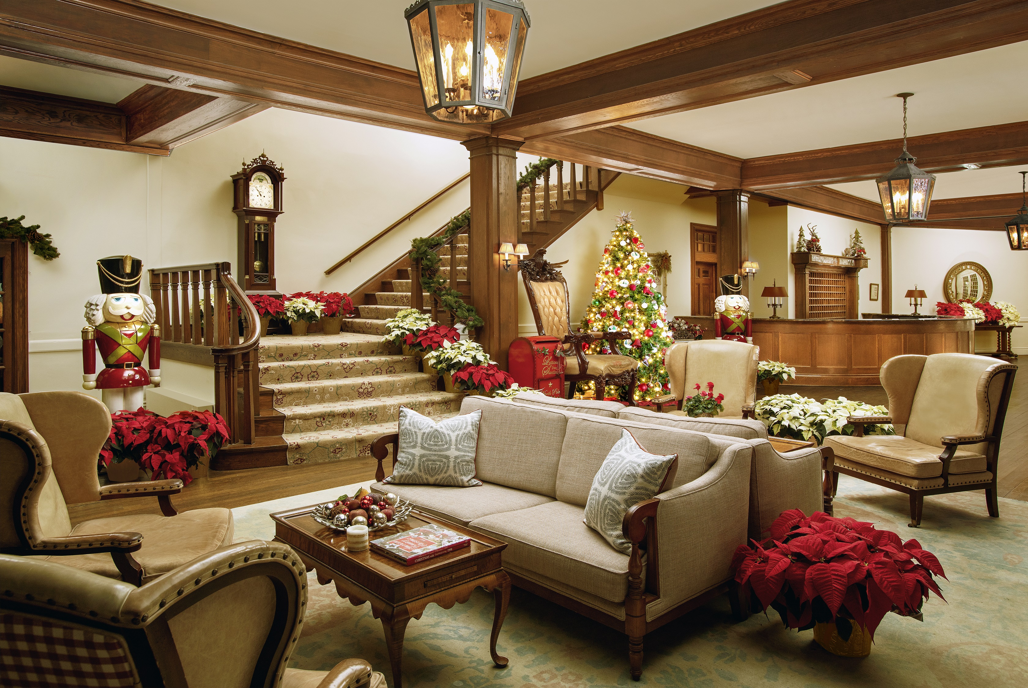 A cozy, festive hotel lobby with a Christmas tree, nutcrackers, poinsettias, vintage furniture, and a carpeted staircase.
