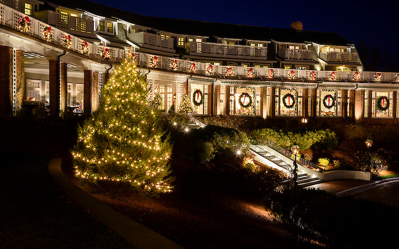 A beautifully decorated building with festive lights and wreaths, featuring a brightly lit Christmas tree in the foreground.