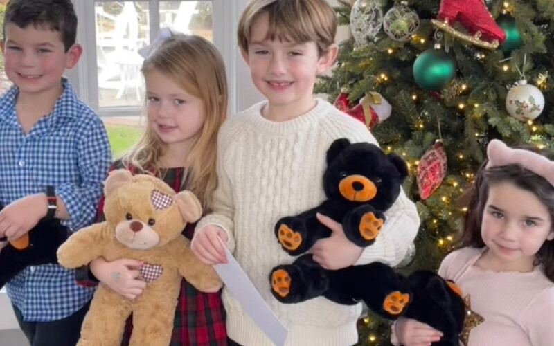 Children smiling near a decorated Christmas tree, holding teddy bears, with festive attire and holiday ambiance.