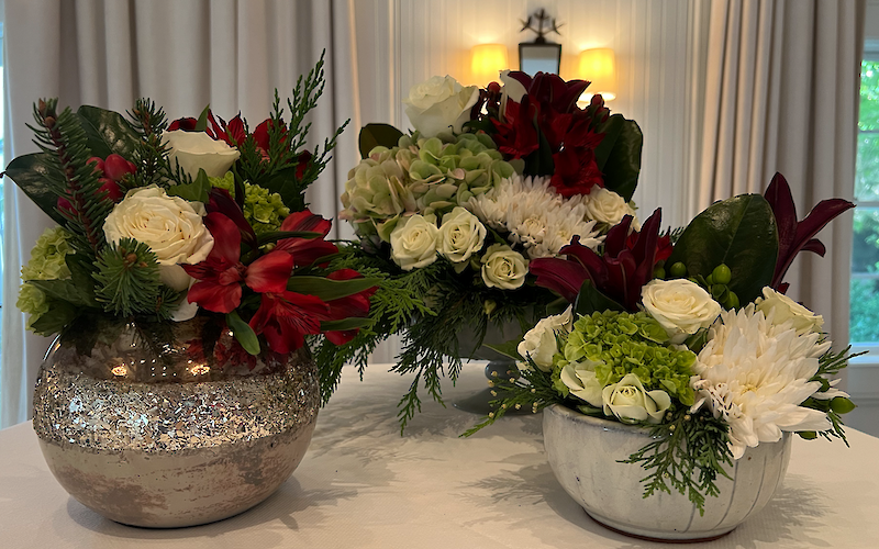 Arrangements of red, white, and green flowers are displayed in rustic vases on a table.
