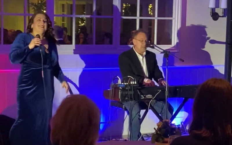 A woman in a blue dress sings with a microphone, while a man plays the keyboard, with colorful lighting.
