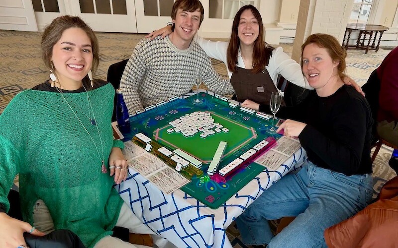 Four people are seated around a table playing Mahjong, smiling and enjoying each other's company.