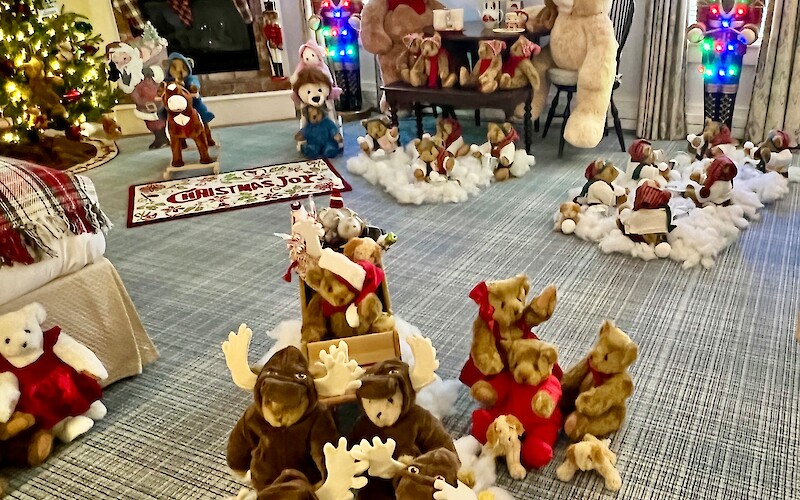 A festive room filled with Christmas decorations, including teddy bears, nutcrackers, a tree, stockings, and plush animals on snowy fluff.