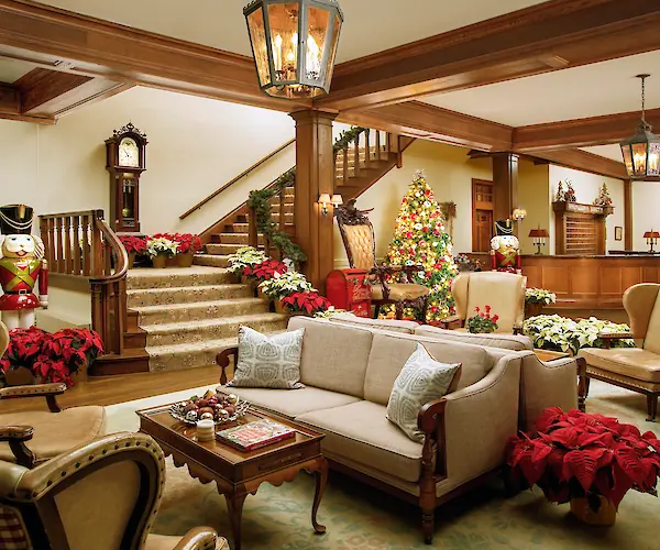 A cozy living area with Christmas decorations, including a tree, nutcracker figures, and poinsettias, featuring a wooden staircase and furniture.