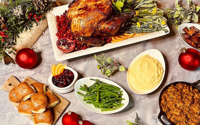 A holiday feast with roast turkey, mashed potatoes, green beans, bread rolls, stuffing, cranberry sauce, and festive decorations.