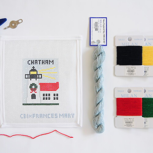 Embroidery setup with a Chatham lighthouse design, yarns in various colors, scissors, and a needle with red thread.