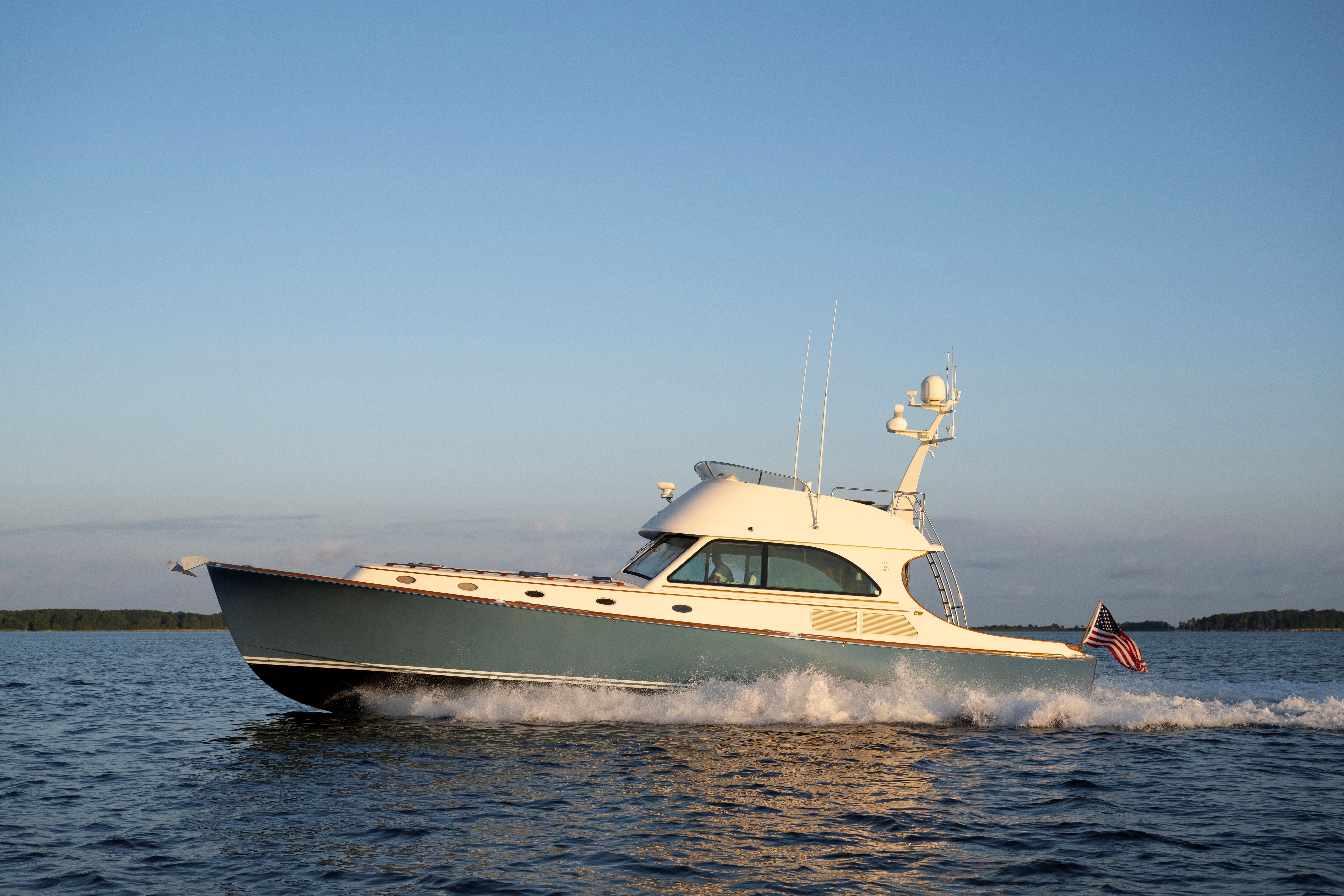 A motor yacht is cruising on the water with the American flag displayed at the back, under a clear blue sky.