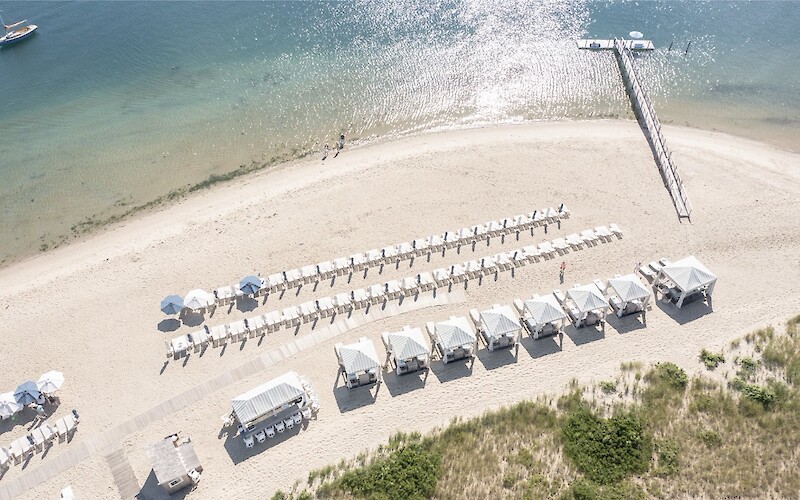 Aerial view of a beach with rows of chairs, cabanas, a boardwalk, and a pier extending into the water.