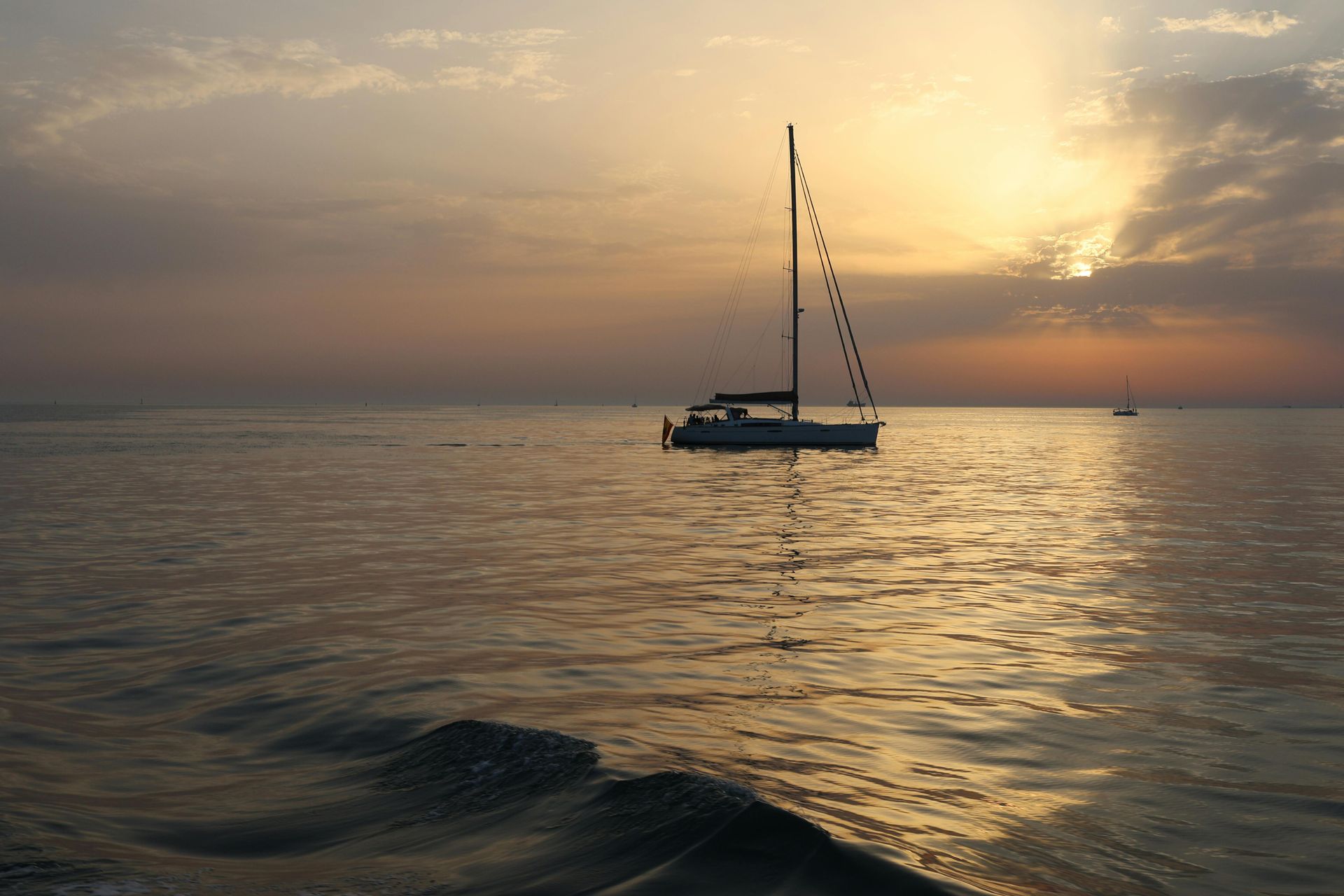 A sailboat on calm waters during a serene sunset, with gentle waves and a peaceful horizon.